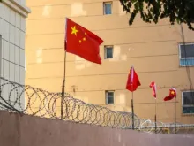 أعلام صينيّة على جدار تعلوه أسلاك شائكة في كاشغر (كاشي)، شينجيانغ-الصين