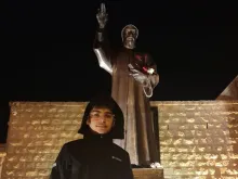جوفن بدران يقف أمام تمثال القديس شربل مخلوف في عنّايا